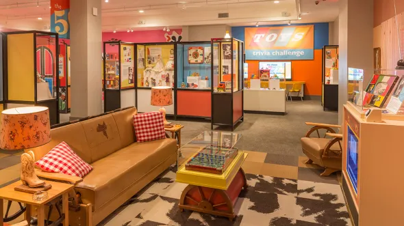 An exhibition display designed like a 1950s living room with couch, coffee and side tables, tv, and rug from the decade