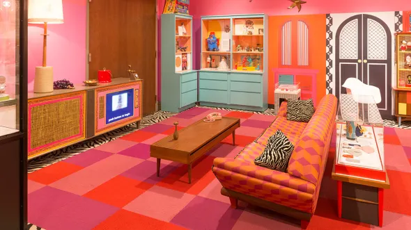 An exhibition display designed like a 1960s living room with couch, coffee and side tables, tv, and rug from the decade