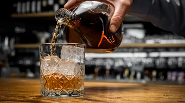 A hand pouring whiskey into a glass with ice