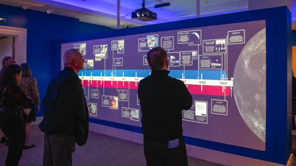 People look at a screen with a timeline of early space exploration in a gallery