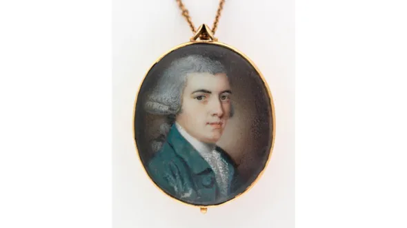 A locket with a portrait of a young white-haired man in a teal waist coat