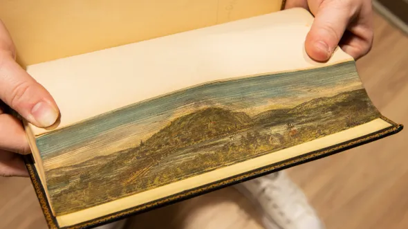 Pages ruffled apart show a painted landscape 