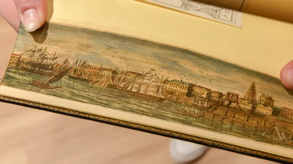 Pages ruffled apart show a painted city and sailing ships on water