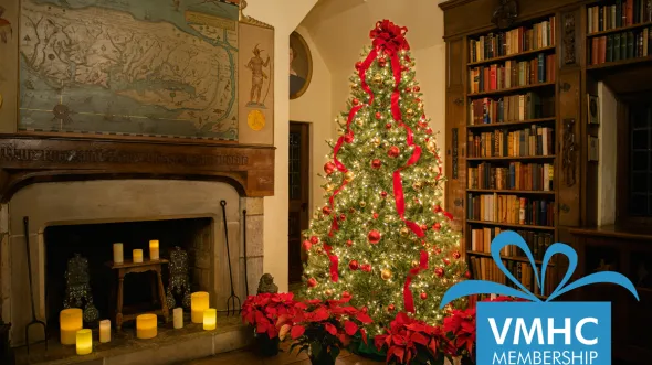 A home library with shelves of books, candles in a fireplace, and a Christmas tree and poinsettias
