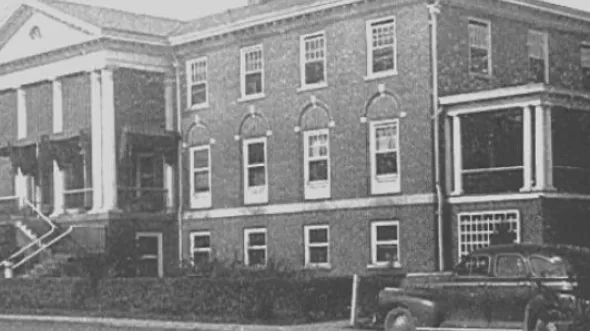 A black and white photo of a columned three story brick building