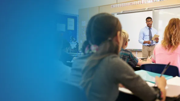 A classroom with students seated at desks and a teacher at the front of the room.