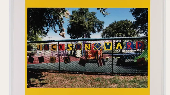 A photograph of painted letters on a chain link fence that spell out Jackson Ward