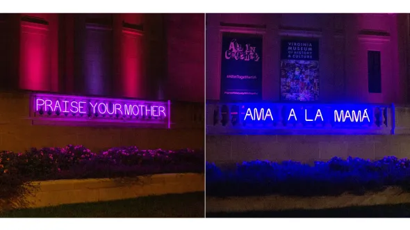 The front of the museum at night illuminated by two neon signs spelling out "Praise Your Mother / Ama A La Mama" in blue and purple.