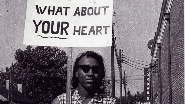 A historic photo of a protester marching with a sign that says "What About Your Heart"