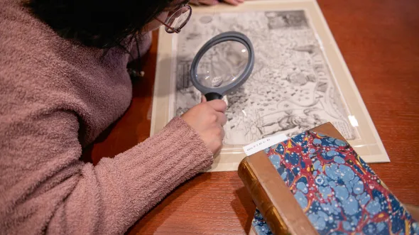 Research A woman looks at a map through a magnifying lense