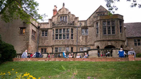 A historic tudor mansion with people milling about on the patio in front of it