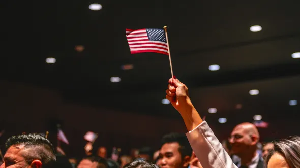 A person holds up a miniature American flag in a crowded auditorium.