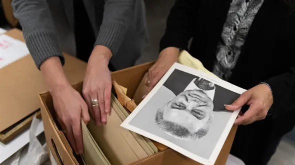 A photo of two sets of hands looking through a file box and holding a black and white photo