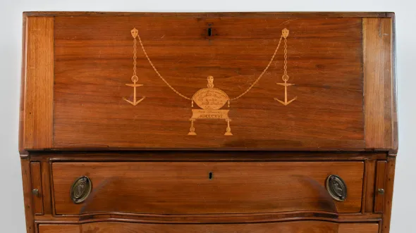 A detail of a wooden rolltop desk with three drawers and a gold scale symbol embossed on the top