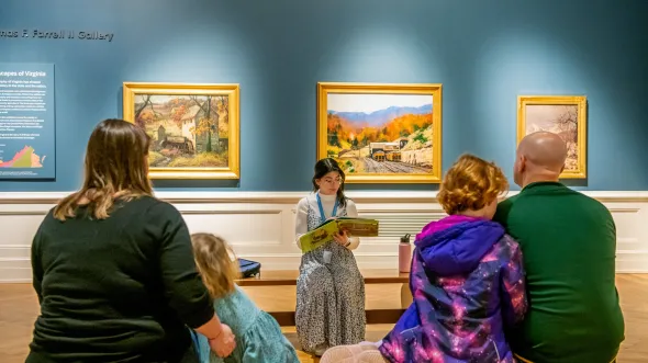 An educator reads a historical story to a family seated in a gallery