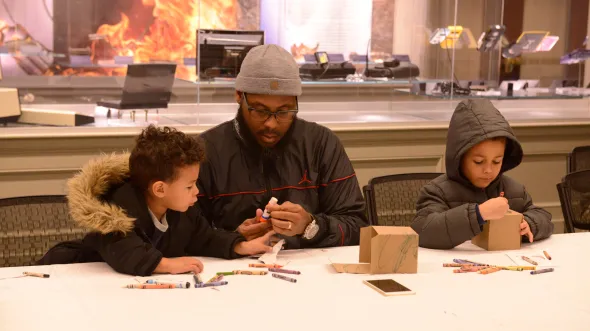An adult and two children do craft activities at a table.