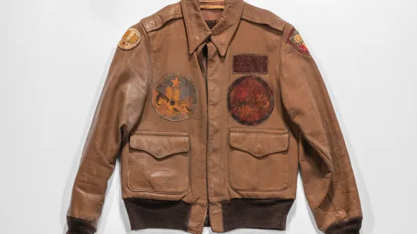A brown leather jacket with sewn patches on the front and a flapped pocket on the bottom left and right sides