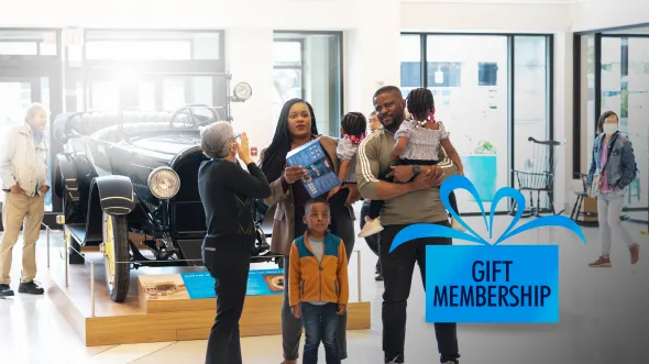 Give the Gift of Membership A family stands in Commonwealth Hall with a large historic car on a platform