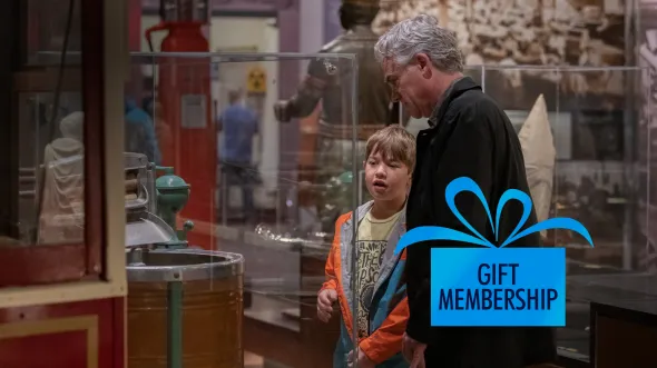 Give the Gift of Membership A man and child look at a display case with a large barrel old-fashioned ice cream maker
