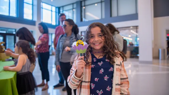 A child smiles while holding a paper craft of a bee in a flower