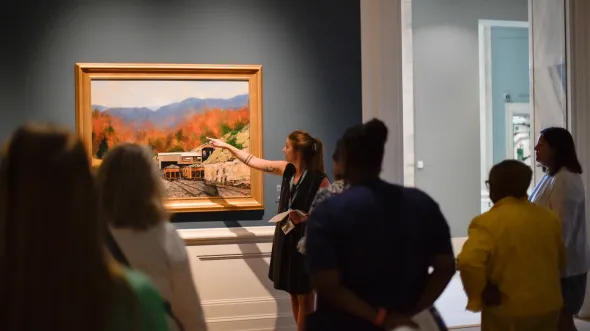 A museum educator points to a landscape painting of Southwest Virginia. 