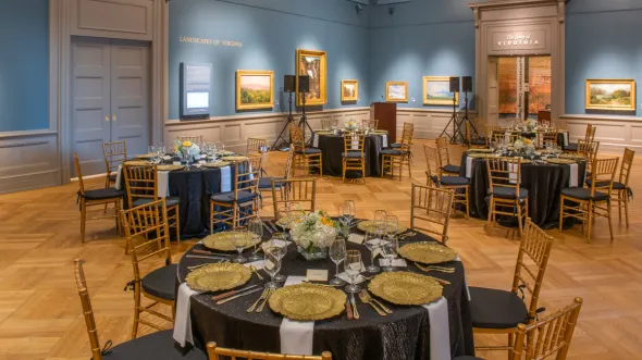 The Olsson Gallery at the VMHC with landscape paintings hanging on walls and dinner tables set for elegant party
