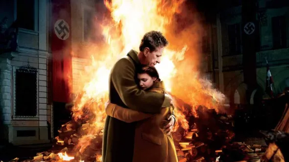 A man and a child embrace in front of a pile of burning books