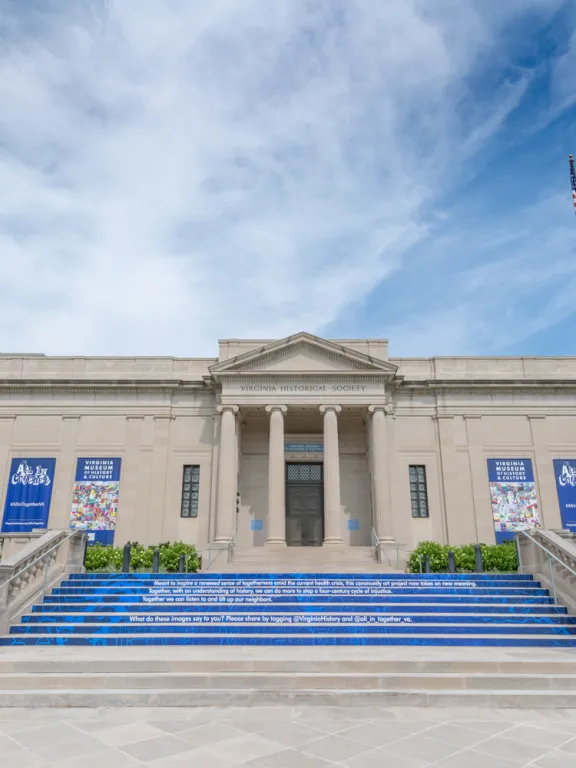 A photo of the front of the museum shows blue artwork on the stairs and blue bannerw with the faces of artists and colorful illustrations.