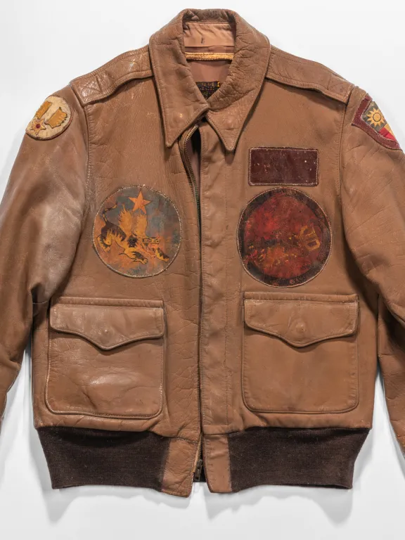 A brown leather jacket with sewn patches on the front and a flapped pocket on the bottom left and right sides