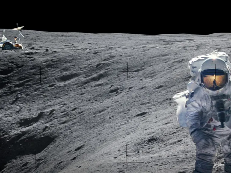 An astronaut in a space suit on the surface of the moon with a lunar rover in the background