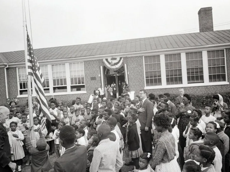 A black and white photo of adults and children outside of a school