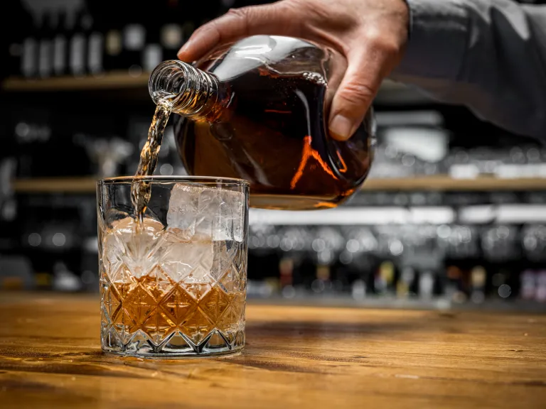 A hand pouring whiskey into a glass with ice