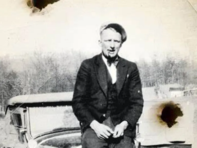 A black and white photo of a man sitting on a car hood.