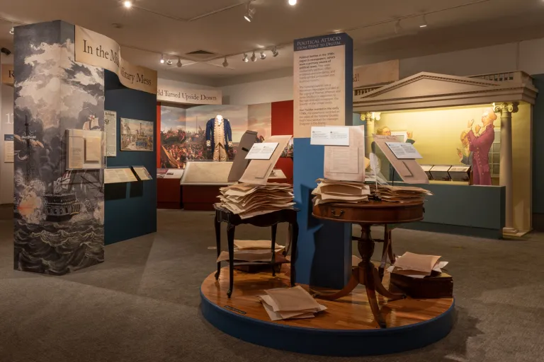 Gallery with display of papers stacked on desks and uniform in background