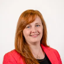 A woman with red hair wearing a black t-shirt and coral blazer