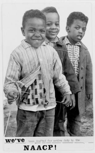 Black and white photograph of three young black boys smiling towards the camera with the words, “we’ve been drafted for active duty by the NAACP!” below.     