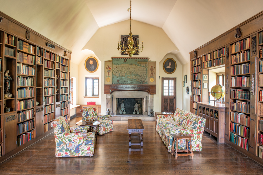 Library showcasing hard wood floors, bookshelves lining each wall, and floral pattered furniture.  