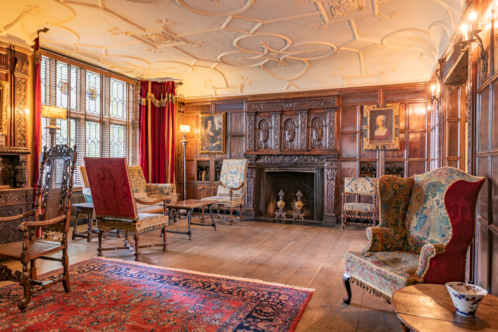 Withdrawing Room  showcasing hard wood floors, decorative rugs and curtains, and an oak fireplace with intricate woodwork detailing. 